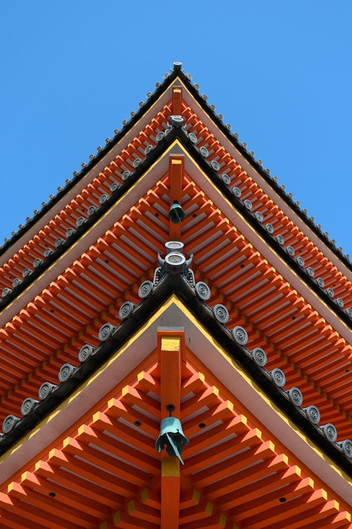 A bottom up view of a pagoda in Kyoto, Japan, that displays vibrant warm colors against a complimentary blue sky background.