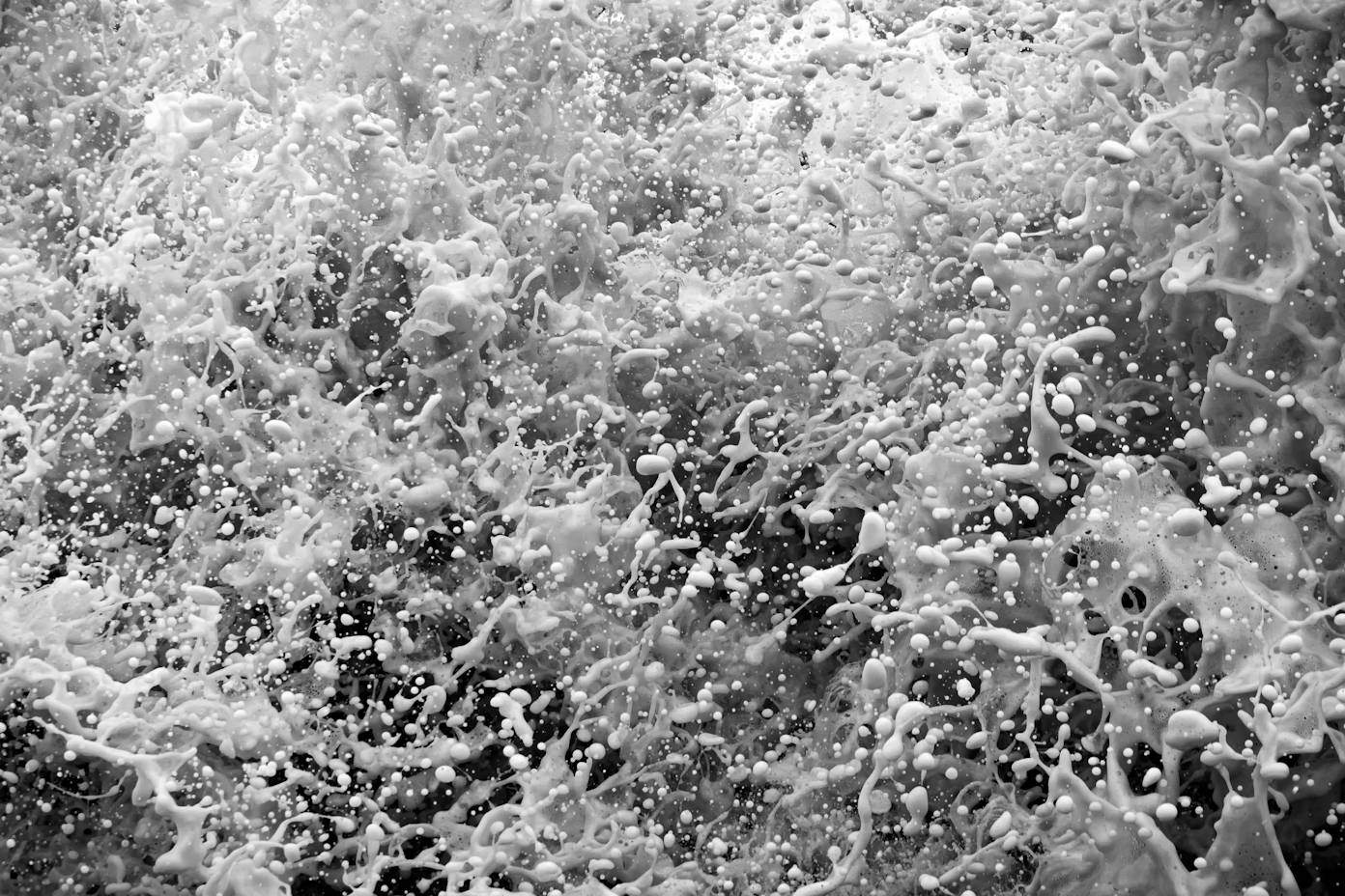 Abstract close-up photograph of sea foam and ocean spray in black and white, featuring intricate textures and dynamic movement.