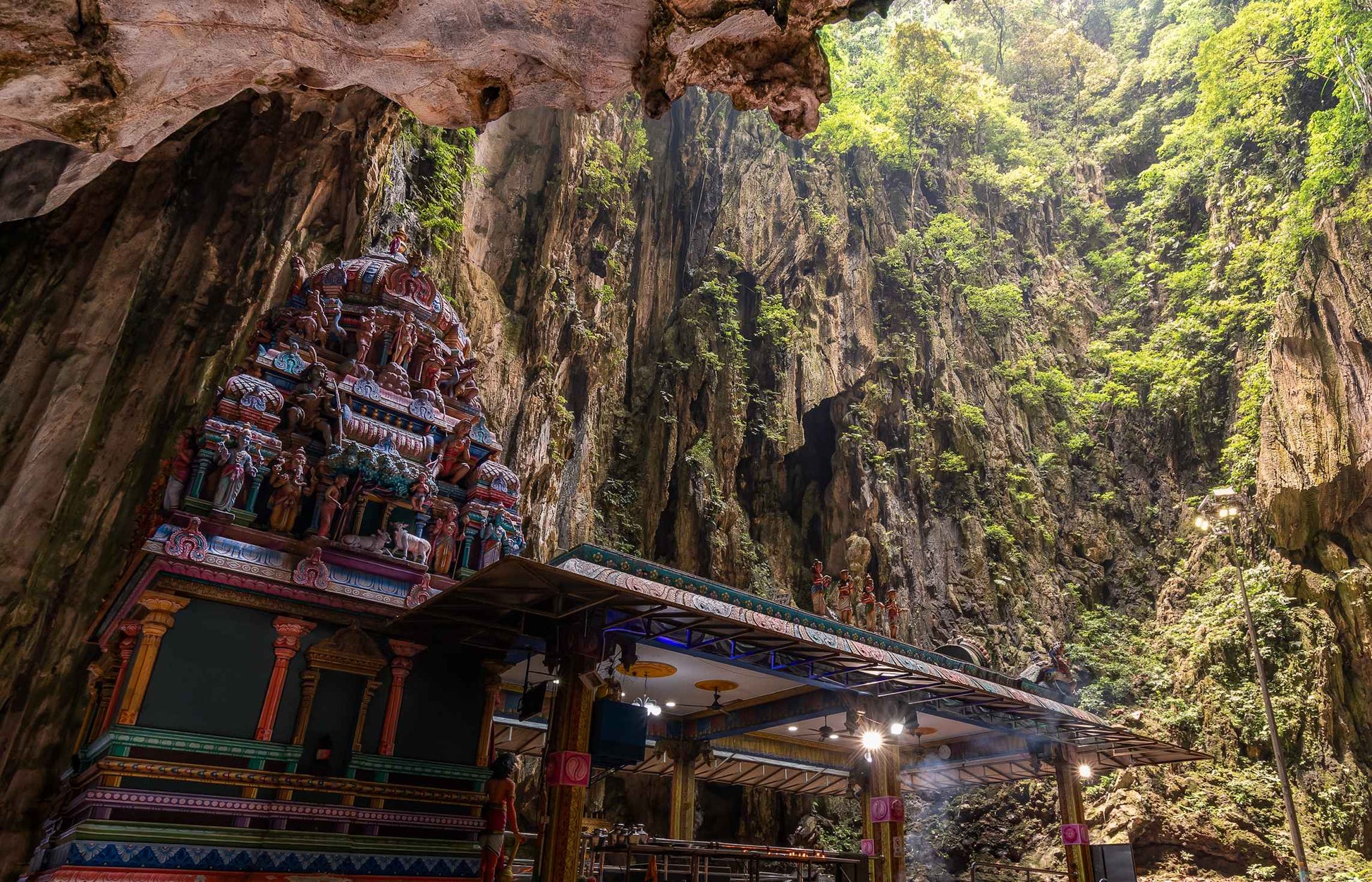 Inside Batu Caves temple complex in Malaysia showing colorful Hindu shrine beneath towering limestone cliffs and lush greenery