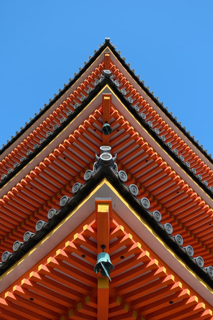 A bottom up view of a pagoda in Kyoto, Japan, that displays vibrant warm colors against a complimentary blue sky background.